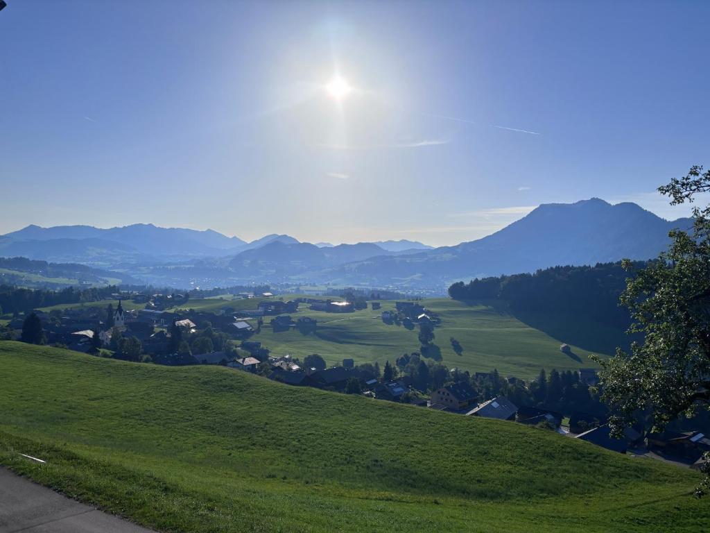 a view of a green hill with the sun in the sky at Panoramazimmer im Bregenzerwald in Schwarzenberg