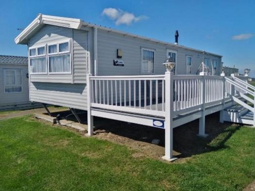 a mobile home with a white porch and a fence at Lymington in Leysdown-on-Sea