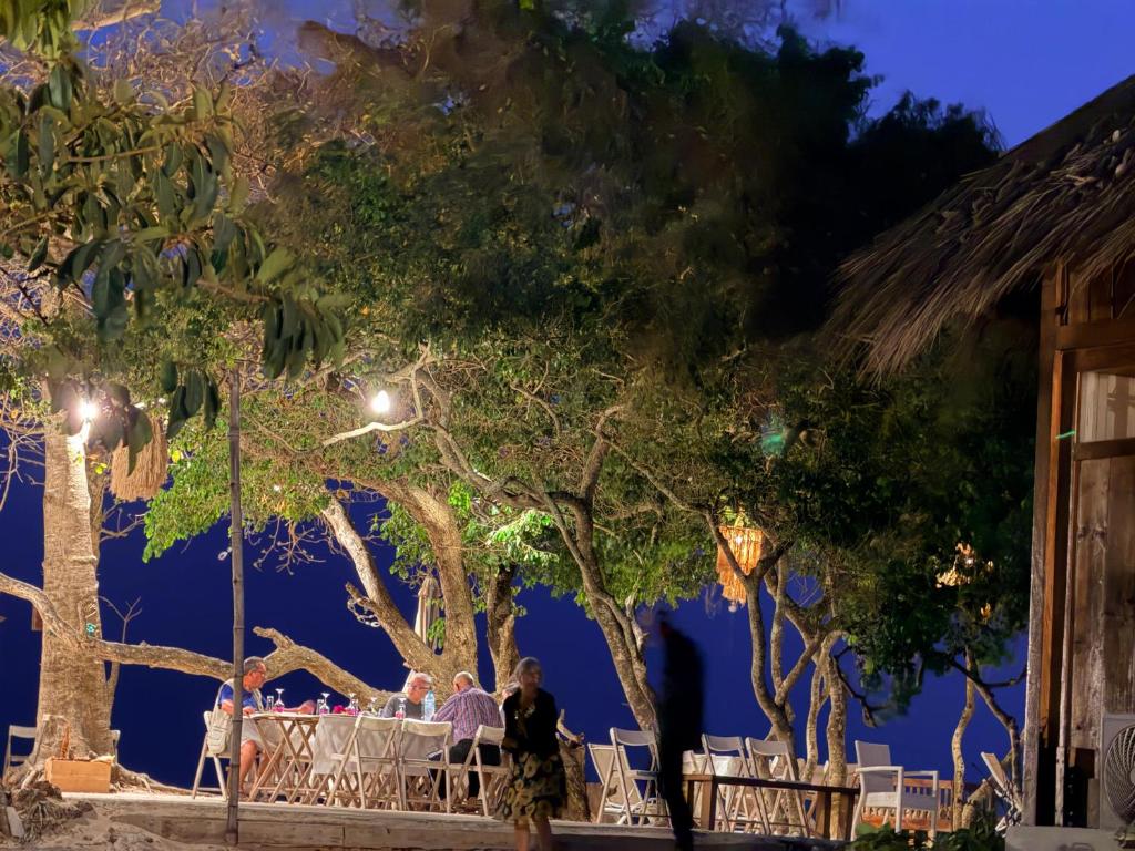 a group of people sitting at tables under trees at night at Anchaca Sul in Bubaque