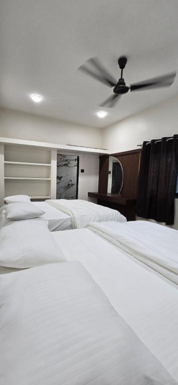 a bedroom with white beds and a ceiling fan at Tuljapur Bhaktaniwas in Tuljapur
