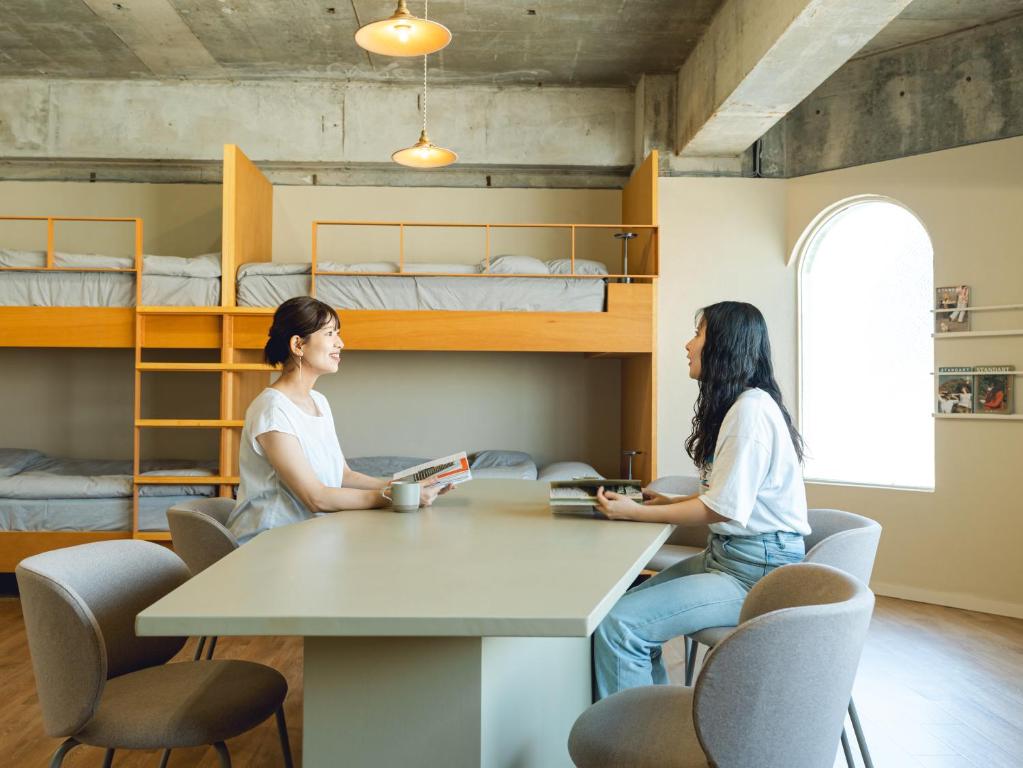 two women sitting at a table in a room with bunk beds at By The Tree Room in Amami