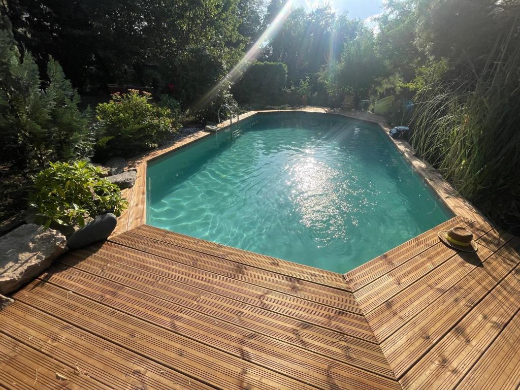 a swimming pool with a wooden deck and the sun shining at Maison avec accès piscine partagée in Colmar