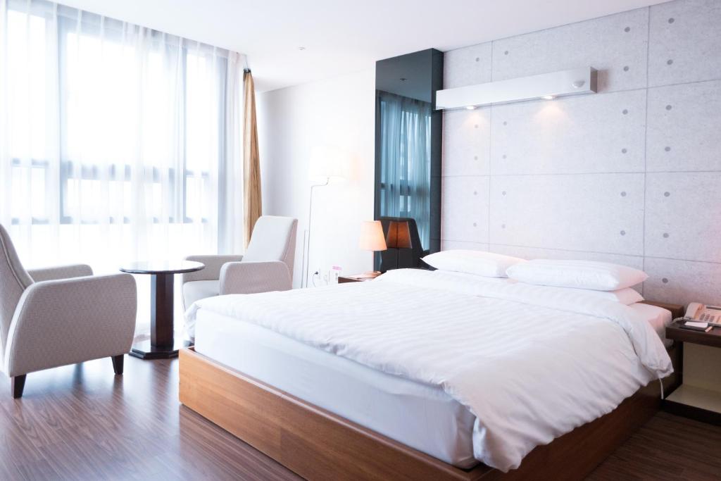 1 dormitorio con 1 cama blanca grande, mesa y sillas en Sunset Business Hotel, en Busan