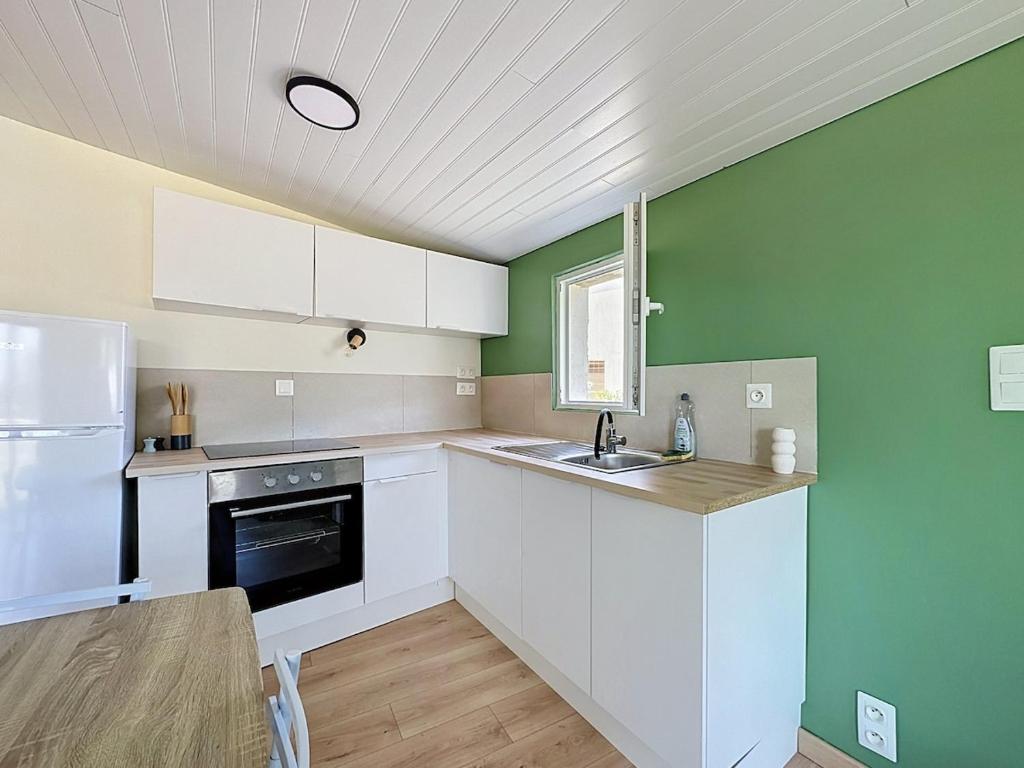 a kitchen with white cabinets and a green wall at Maisonnette avec jardin privé in Secondigny