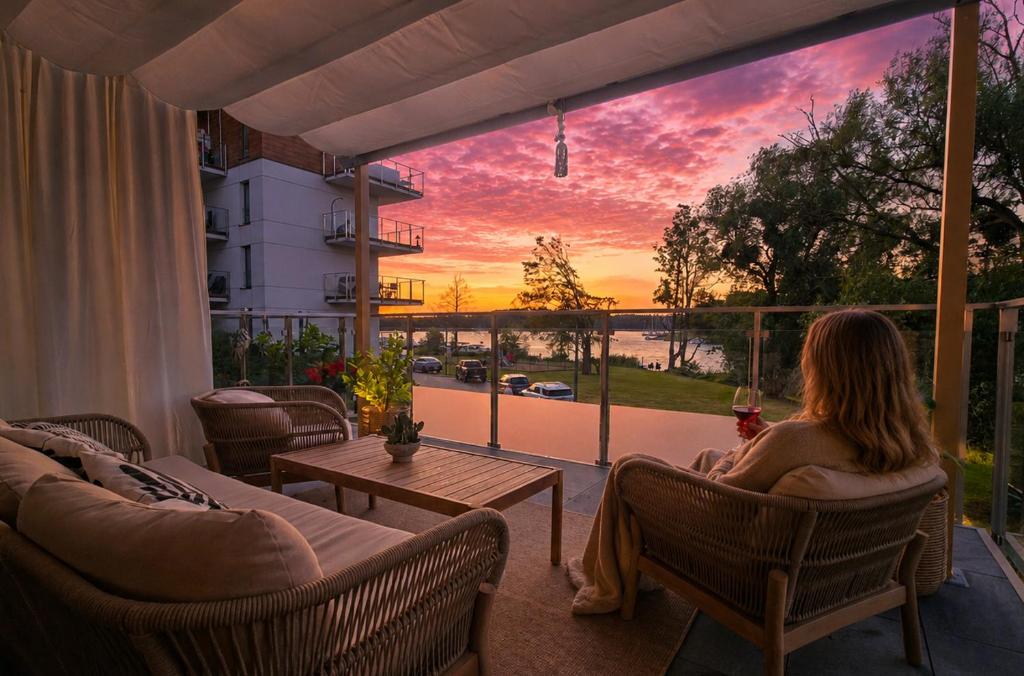 a woman sitting on a porch watching the sunset at Porto Marina - widok na jezioro z każdego z 3 pokoi, lux, garaż, klima in Iława