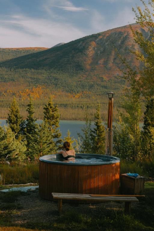 a woman sitting in a hot tub with a view of a lake at CabinsOver Crag Lake Glamping Bear in Carcross