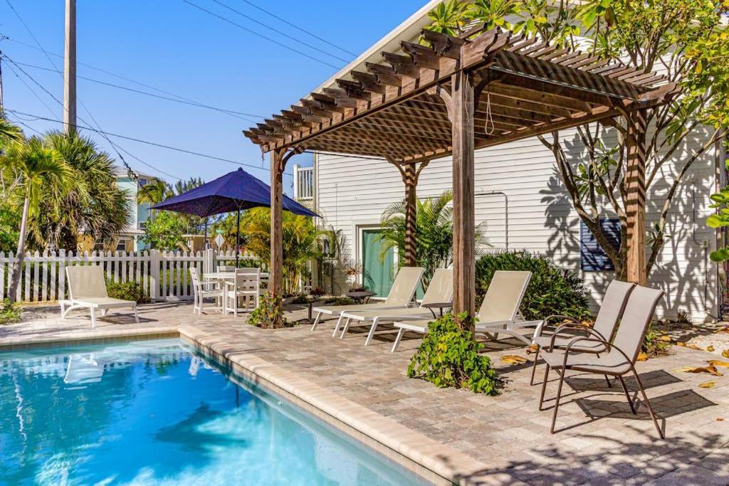 a swimming pool with chairs and a pergola next to a house at Sundance Cottage in Anna Maria
