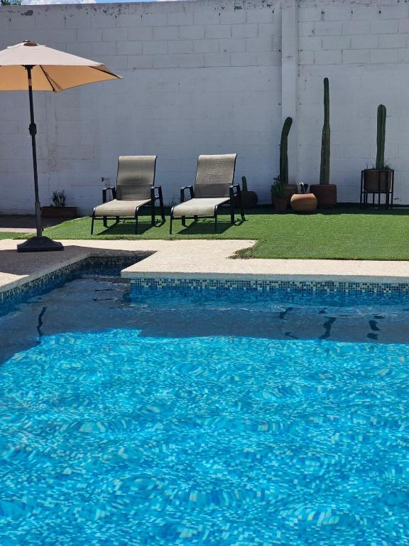 a swimming pool with two chairs and an umbrella at Alberca Privada a 15min del centro de la ciudad in Chihuahua