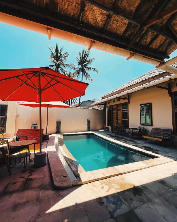 a swimming pool with a red umbrella and a table at La Boheme Mini in Gili Trawangan