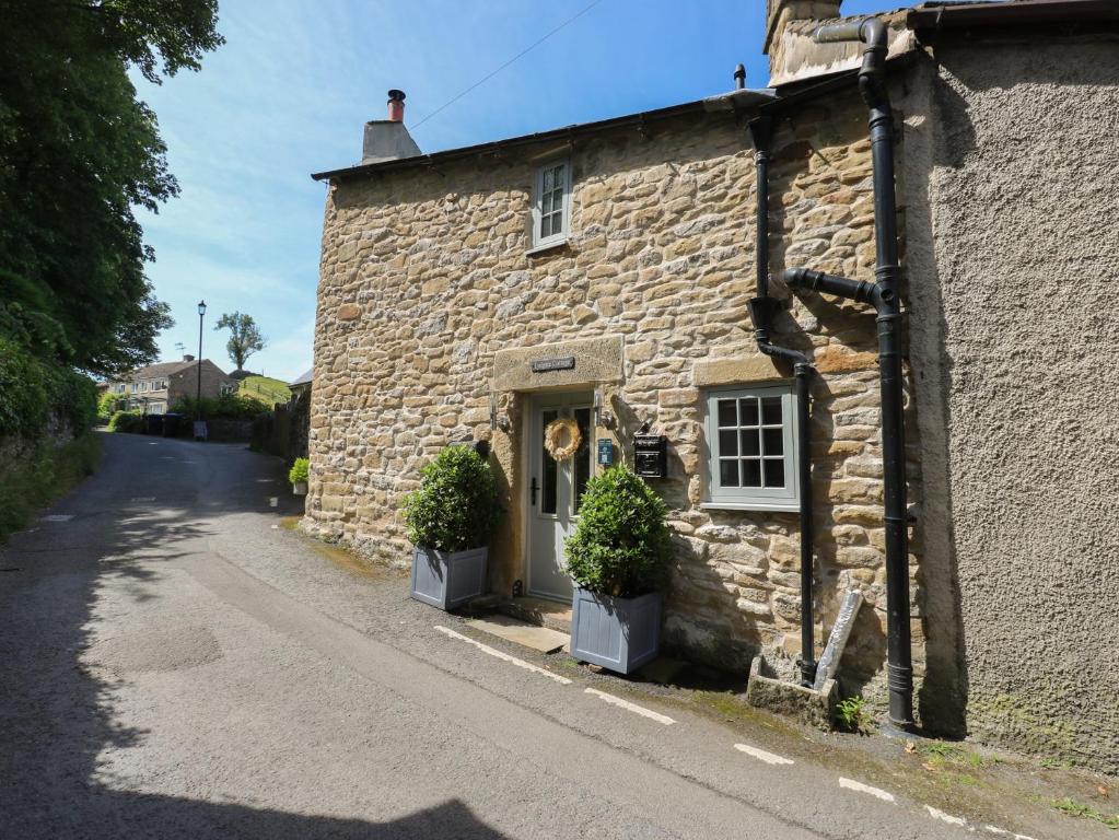 a stone building with two plants in front of it at Lydgate Cottage in Eyam