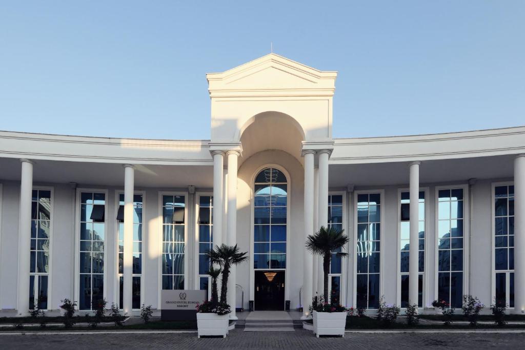 a white building with palm trees in front of it at Velipoja Grand Europa Resort, Affiliated by Meliá in Velipojë
