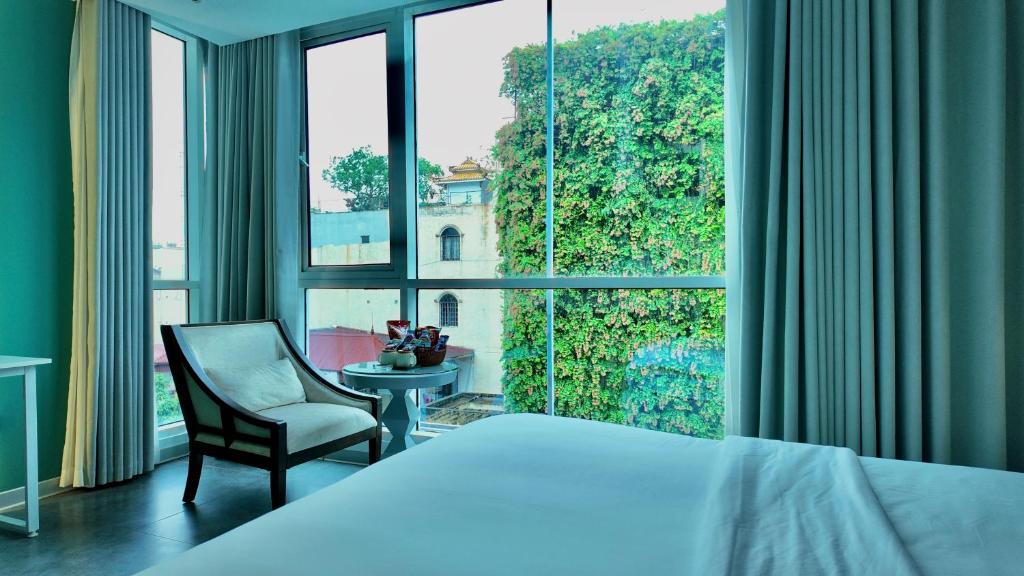a bedroom with a bed and a chair and a large window at J Village Hotel - Triệu Việt Vương in Hanoi