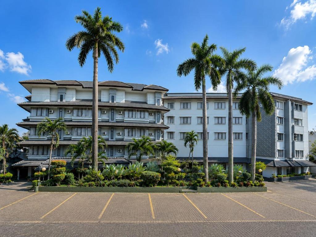 a large white building with palm trees in a parking lot at Citra Boutique Hotel Cikarang in Cikarang