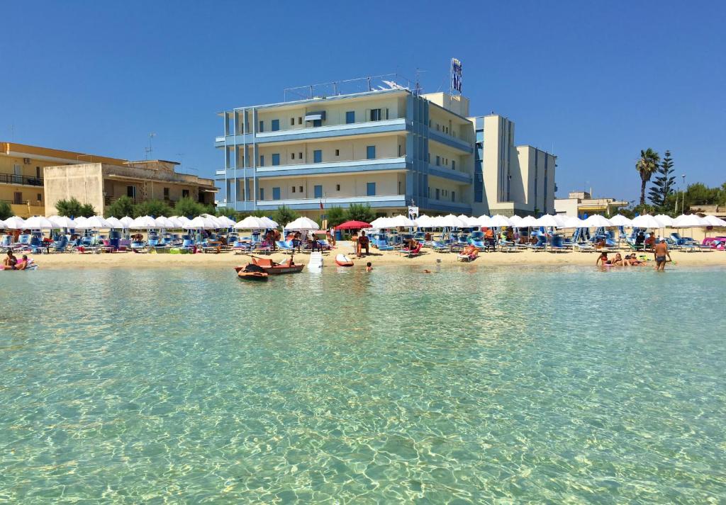 a beach with people in the water and a building at Hotel Blu in Porto Cesareo