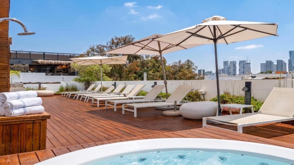 a hot tub on a deck with lounge chairs and umbrellas at Jacob Shenkin Hotel in Tel Aviv
