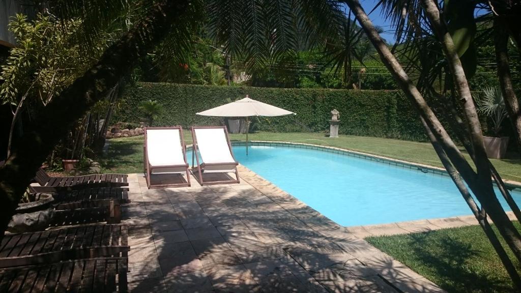 duas cadeiras e um guarda-sol junto a uma piscina em REB Casa Itanhangá no Rio de Janeiro