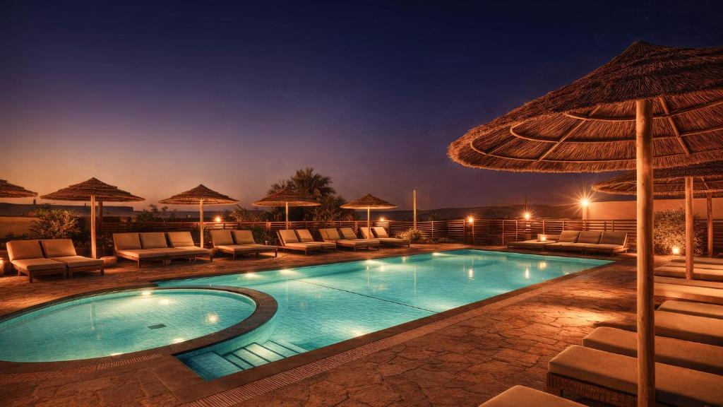 a swimming pool with chairs and an umbrella at night at Jacob Mitzpe Ramon in Mitzpe Ramon