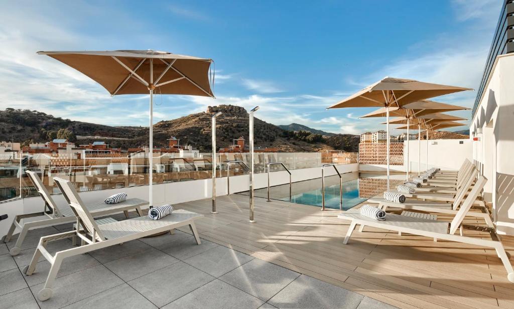 a rooftop patio with chairs and umbrellas on a building at Sercotel Rosaleda Málaga in Málaga