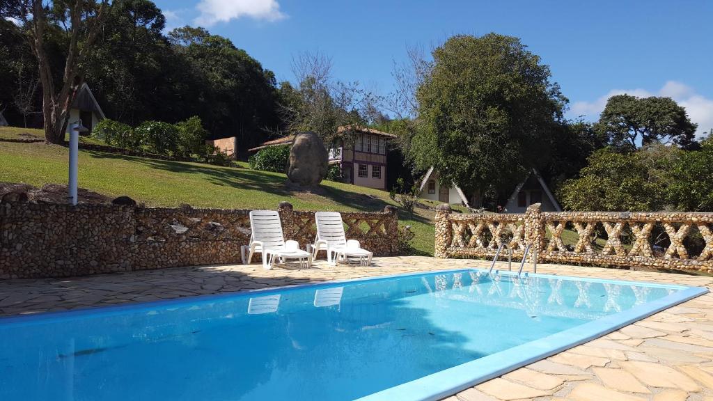 a swimming pool with two chairs and a house at Pousada Meu Recanto in Conceição da Ibitipoca