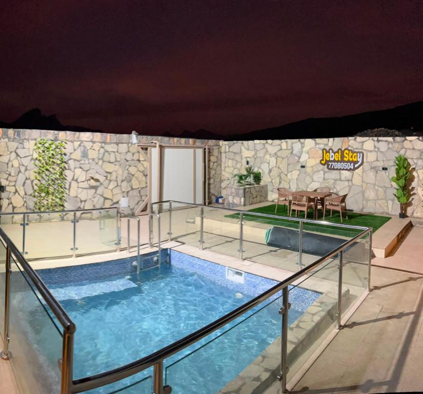 a swimming pool with a table and a stone wall at JebelStay in Al Ḩamrāʼ