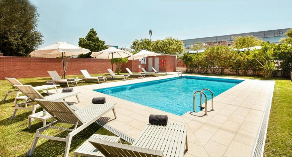 a swimming pool with lounge chairs and a table and a pool at Sercotel Sant Boi in Sant Boi del Llobregat