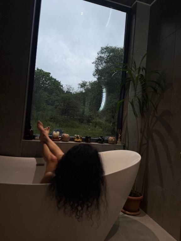 a person sitting in a bath tub looking out a window at "The Nest" Premium Mountain Lodge with Alpine retreat & Sauna in Vanadzor