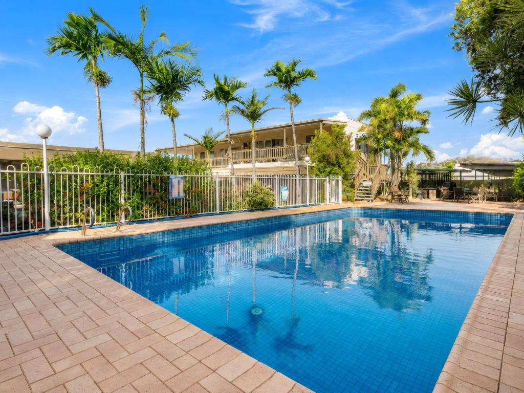 a swimming pool with palm trees and a building at Gladstone CBD Motel in Gladstone