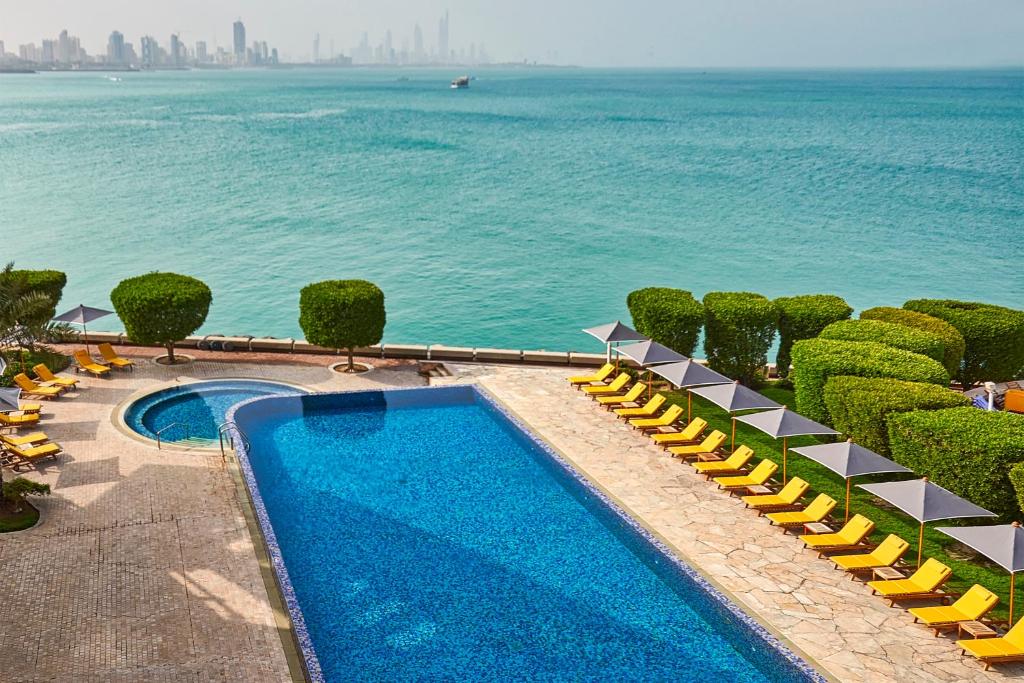 a swimming pool next to the water with yellow lounge chairs at Marina Hotel in Kuwait