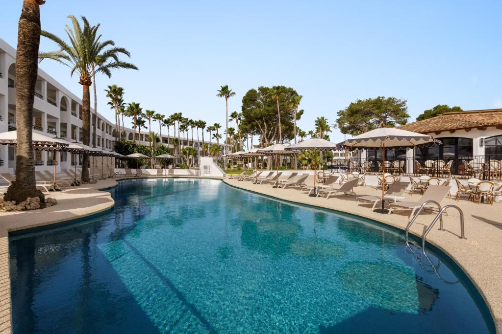 a swimming pool at a resort with chairs and palm trees at Wyndham Mallorca Portocolom Resort in Portocolom