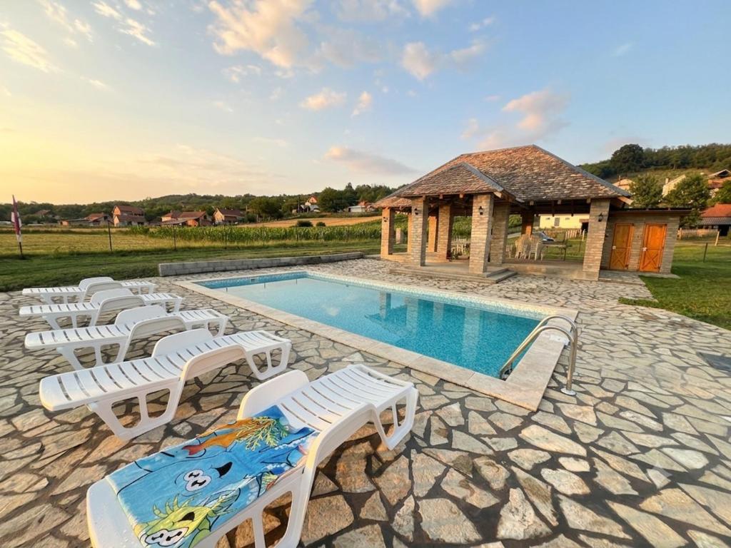 a swimming pool with white chairs and a gazebo at Čajića avlija pool house in Obrenovac