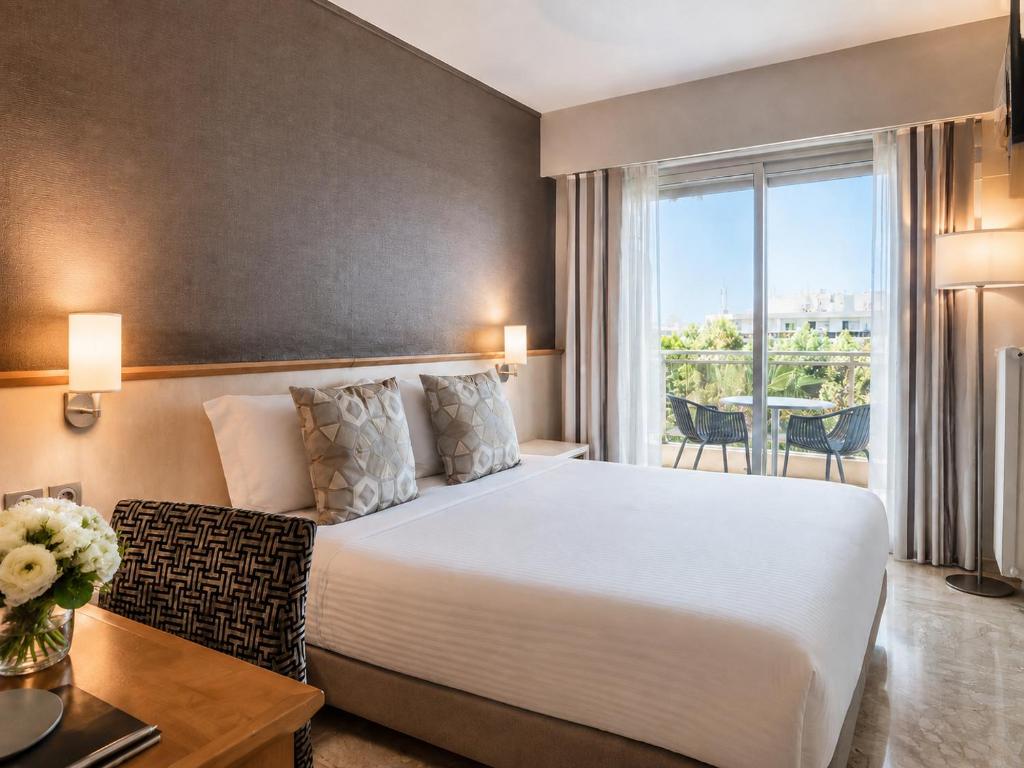 a hotel room with a bed and a table and a window at The Originals Boutique, Hôtel Les Strélitzias in Juan-les-Pins