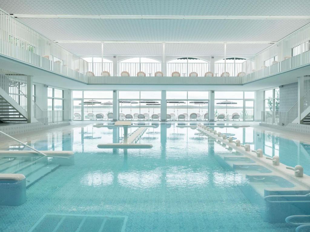 a large pool with tables and chairs in a building at Bel Hôtel Oléron Thalasso & Spa - MGallery Collection in Saint-Trojan-les-Bains
