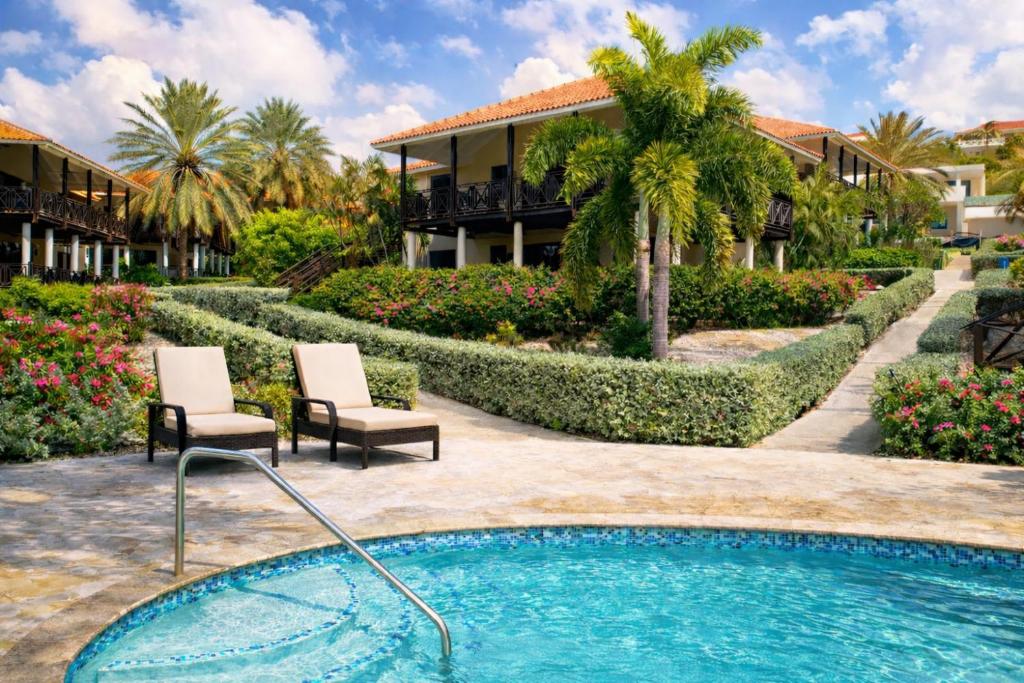a resort with a swimming pool and two chairs at POCO POCO Villa - Poolside Golf & Beachfront Resort in Dorp Sint Michiel
