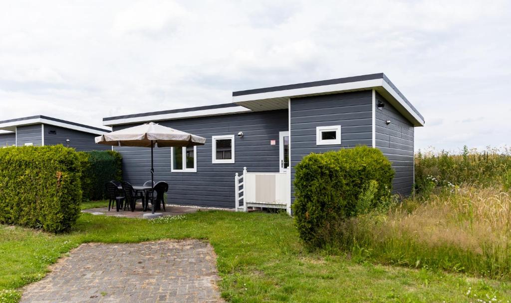 a grey caravan with a table and an umbrella at De Tien Heugten in Schoonloo