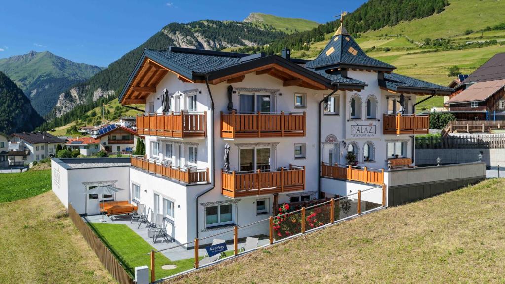 a white house with orange balconies on a hill at Palazi Apartments & Spa - Bike, Ski & Wellness in Nauders in Nauders