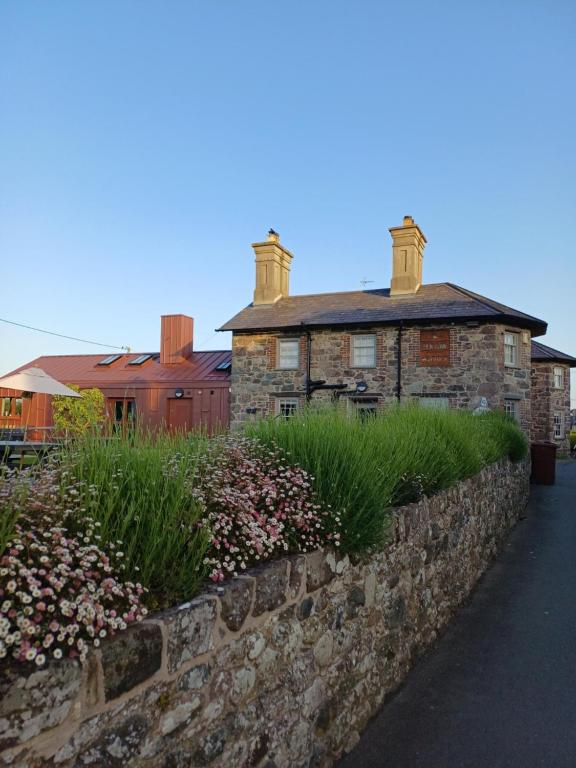 a stone house with a stone wall and some flowers at Ty'n Llan- tafarn gymunedol- community pub in Llandwrog