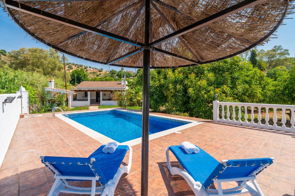 a patio with two chairs and an umbrella next to a swimming pool at Cubo's Charming House Las Millanas in Tolox