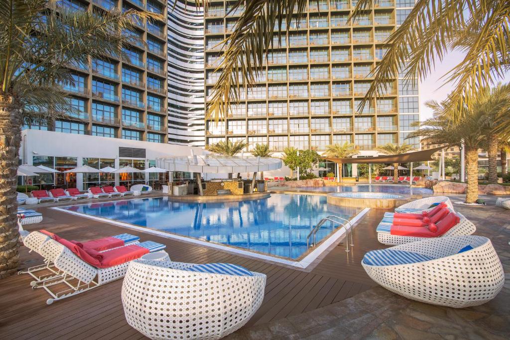 ein Hotelpool mit Stühlen und ein großes Gebäude in der Unterkunft Yas Island Rotana Abu Dhabi in Abu Dhabi