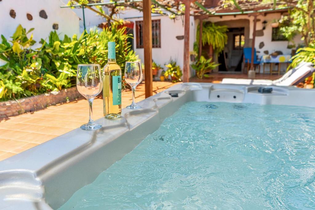 two wine glasses and wine bottles sitting next to a hot tub at Casa Rural Guiniguada in Santa Brígida