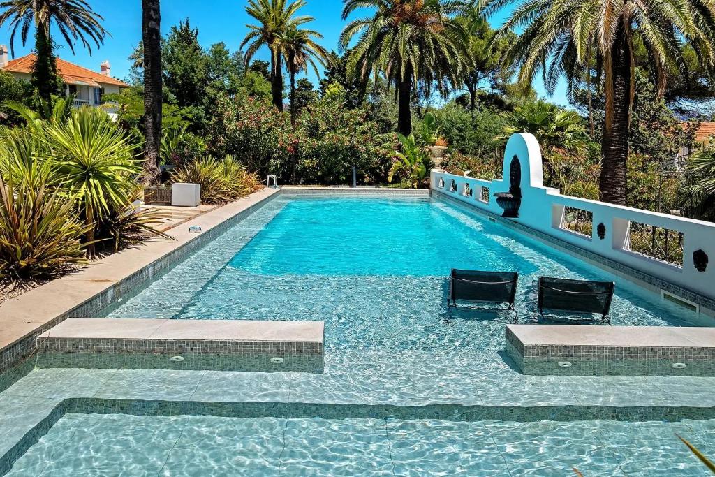 a swimming pool with two chairs and palm trees at Villa Belle Epoque Saint-Raphaël in Saint-Raphaël