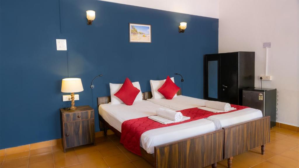 a blue room with a bed with red pillows at Shelter Guest House in Candolim