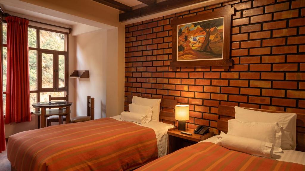 a room with two beds and a brick wall at Andina Principal in Machu Picchu