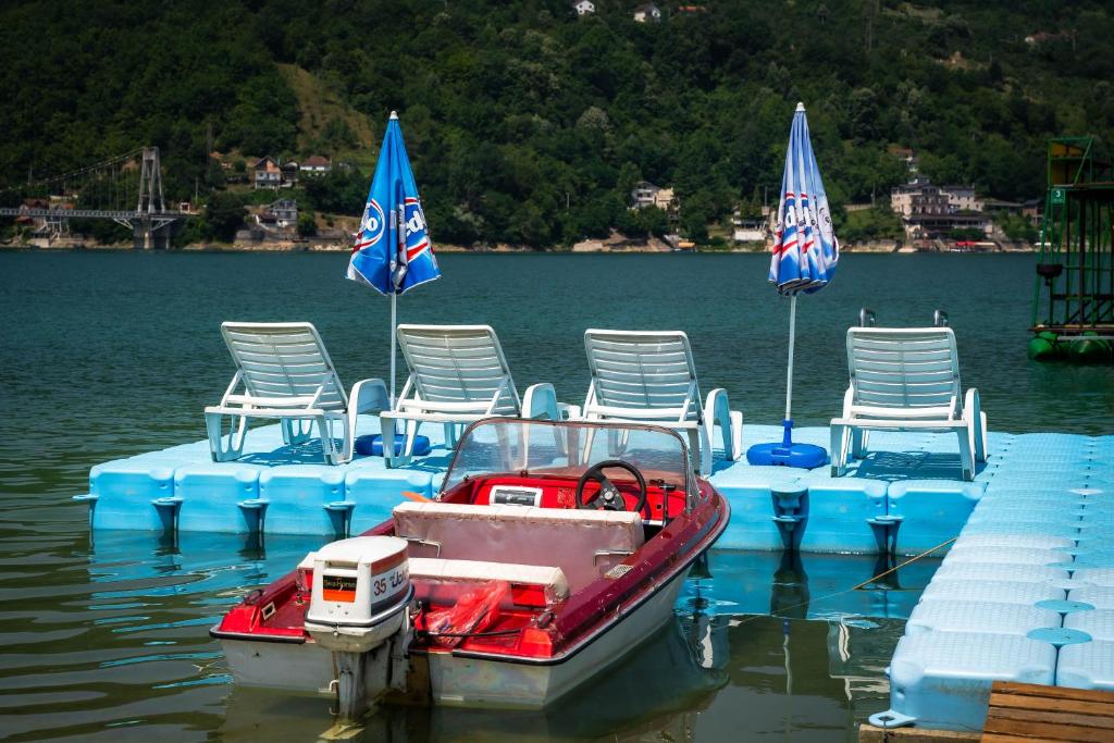 a small boat sitting on the water with chairs and umbrellas at Lakeside Cabin in Jablanica