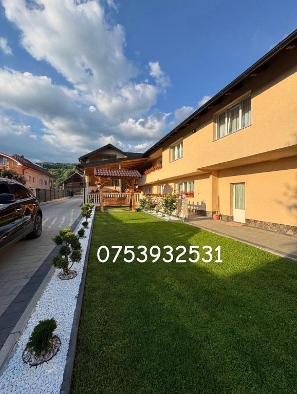 a house with a lawn in front of a building at Pensiunea Edy in Statjunea Borsa