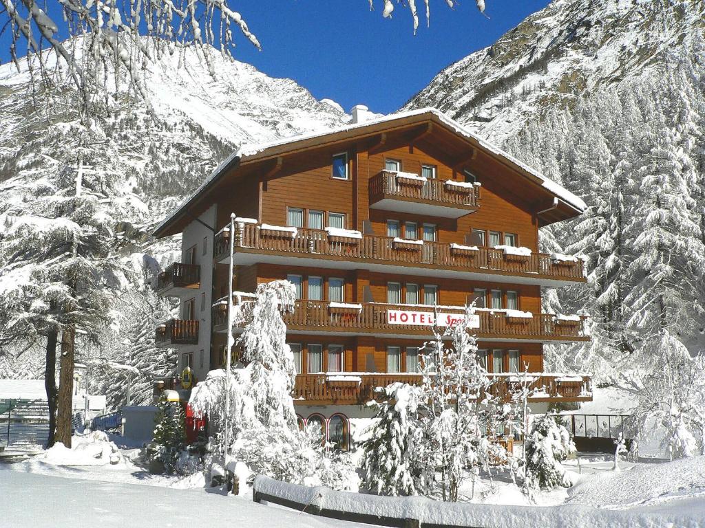 un grand bâtiment en bois dans la neige avec des arbres enneigés dans l'établissement Ski-In/Ski-Out Hotel Sport, à Saas-Almagell