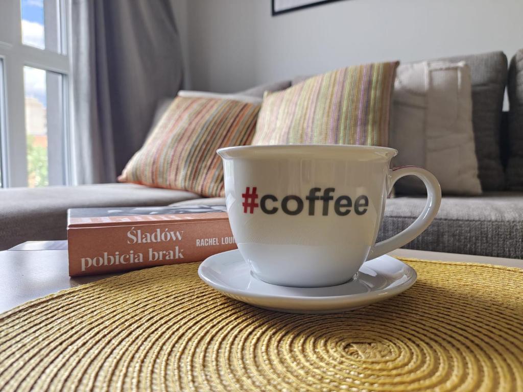 a coffee cup sitting on a table with a book at Apartament Glatz - na Letniej, Kłodzko, winda, garaż podziemny, balkon z widokiem na góry in Kłodzko