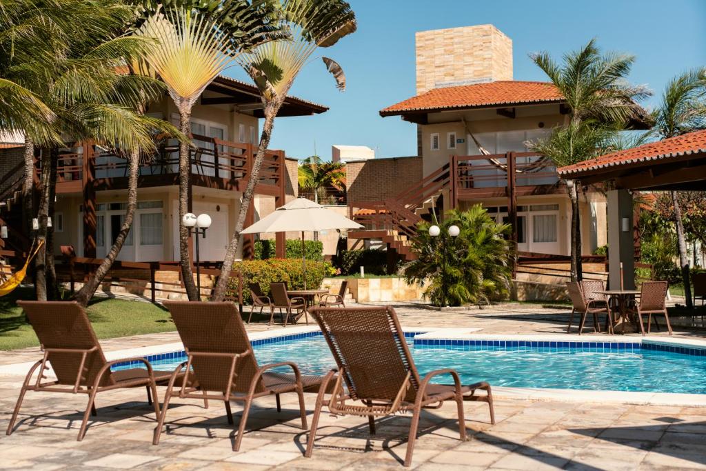 a resort with a pool and chairs and palm trees at Pousada Tropical Ilhas in Aquiraz