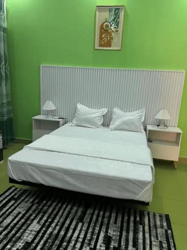 a bedroom with a large white bed with green walls at Hôtel La Parisienne in Louga