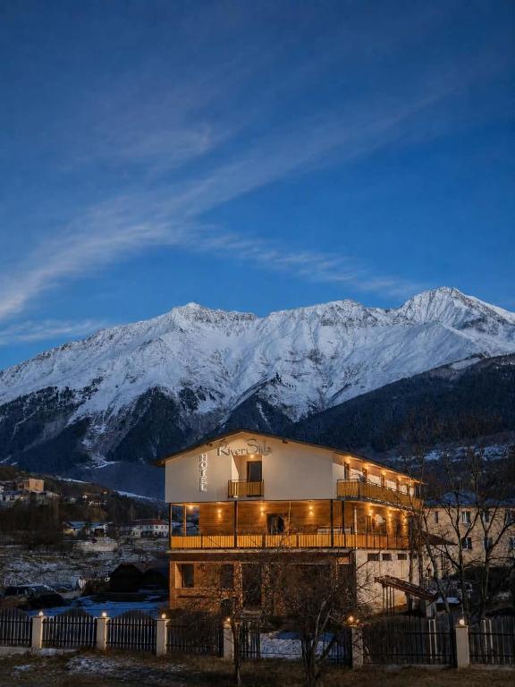 a building with snow covered mountains in the background at hotel "Riverside Mestia" in Mestia