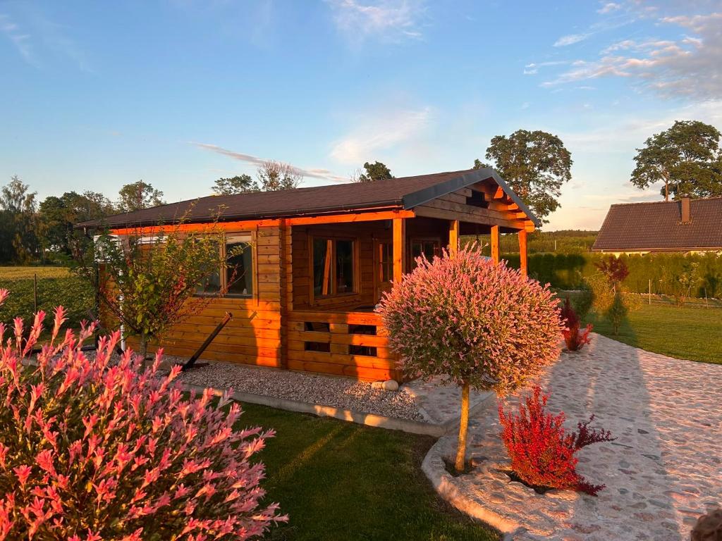 a small wooden cabin in a garden with pink flowers at Domki nad stawem in Sambród